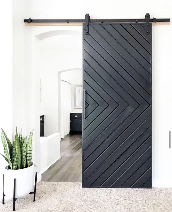 a white space with a black chevron barn door, a planter with greenery and some black furniture to echo with the doors
