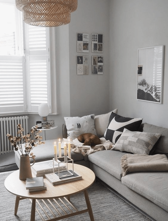 an airy Scandinavian space with a grey sectional sofa, a coffee table, printed pillows, a gallery wall and a woven pendant lamp