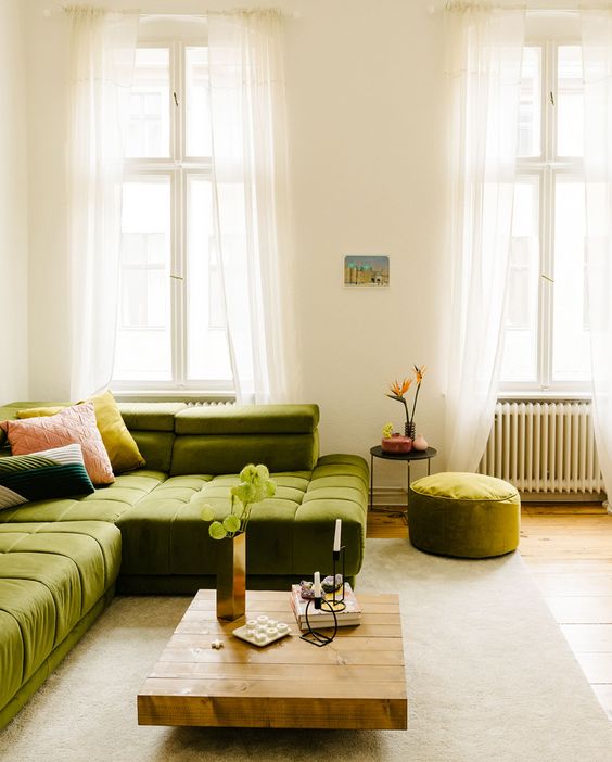 an airy living room with a low green sectional, a low coffee table, a pouf and a side table plus colorful pillows