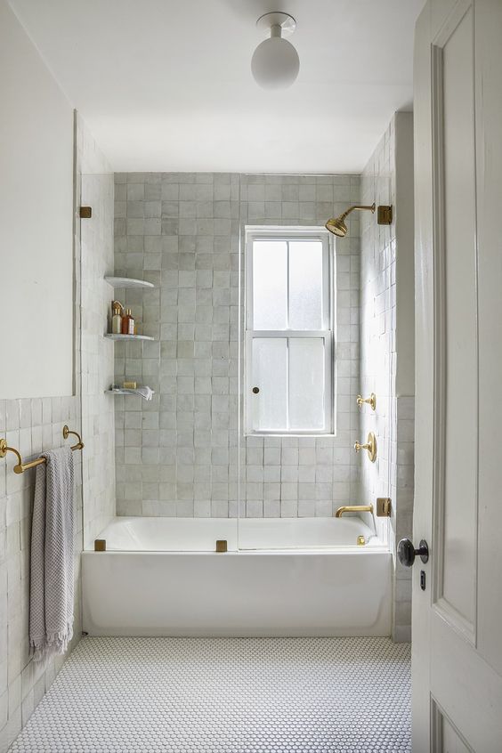 an all-white bathroom made more eye-catchy with Zellige and penny tile, a tub and shelves and gold fixtures