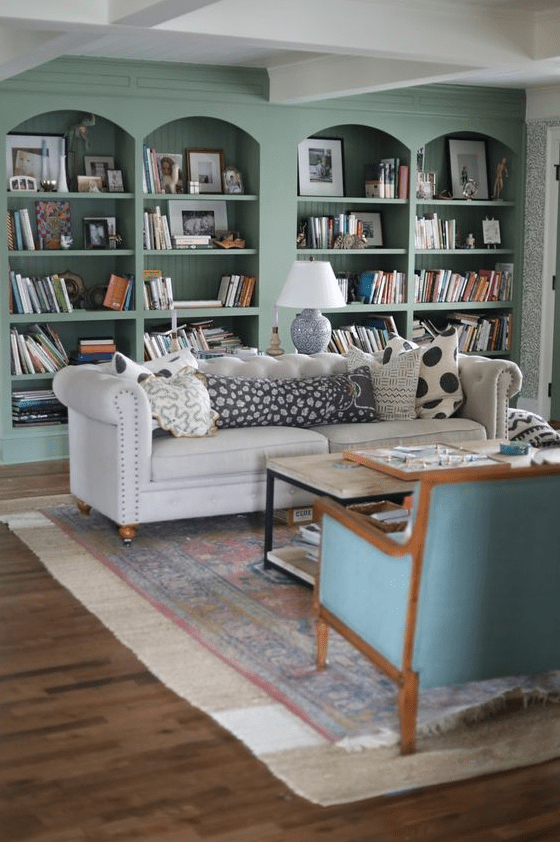 An eclectic living room with built in sage green arched bookcases, a white sofa, some chairs, a coffee table