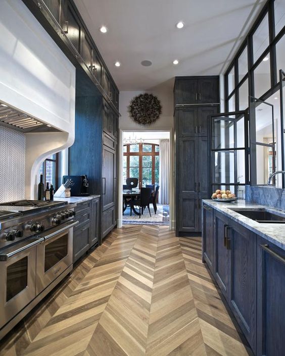 an elegant navy kitchen with chevron floors, a glazed wall, lights and stainless steel appliances is amazing and very refined