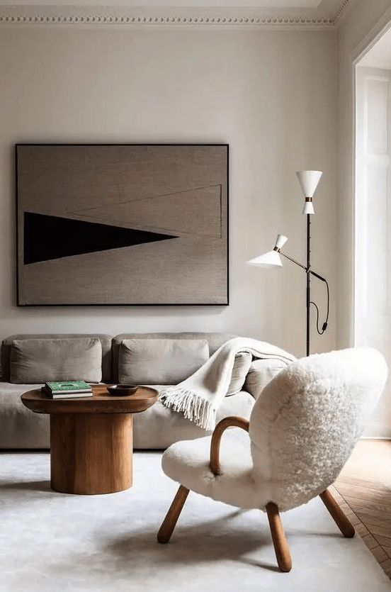 an ethereal Scandinavian living room with a grey low sofa, a creamy chair, a wooden coffee table, a floor lamp and a bold artwork