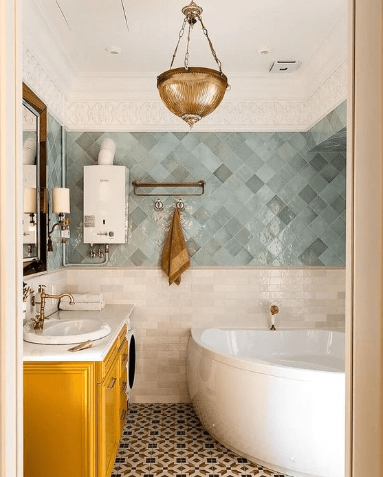 an eye-catchy bathroom done with grey and green Zellige tiles, a corner tub, a yellow vanity, a brass pendant lamp