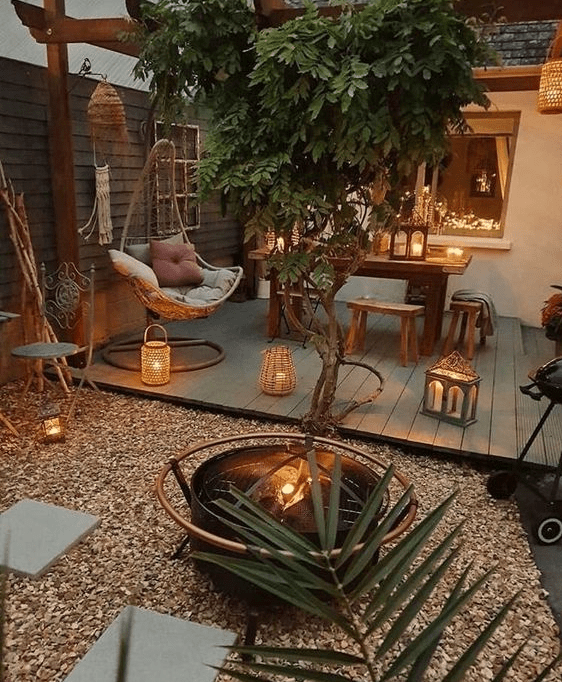 an inviting patio with a wooden dining set, a suspended chair, a fire pit, candle lanterns and lights is wow