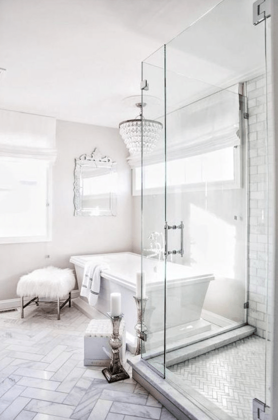 an ornate mirror, a crystal chandelier, a faux fur stool and candles plus marble tiles make the bathroom glam