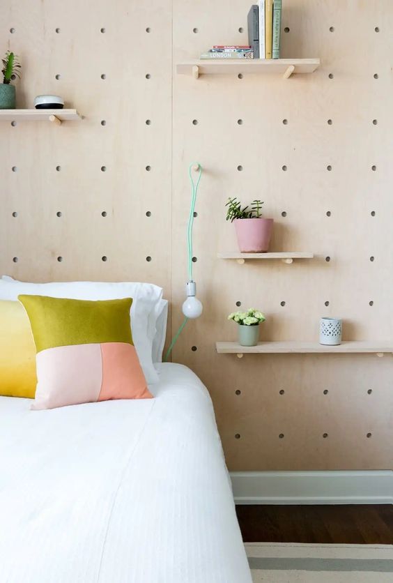 a Scandinavian bedroom with a large pegboard with shelves, some potted plants and pendant bulbs is a cool space