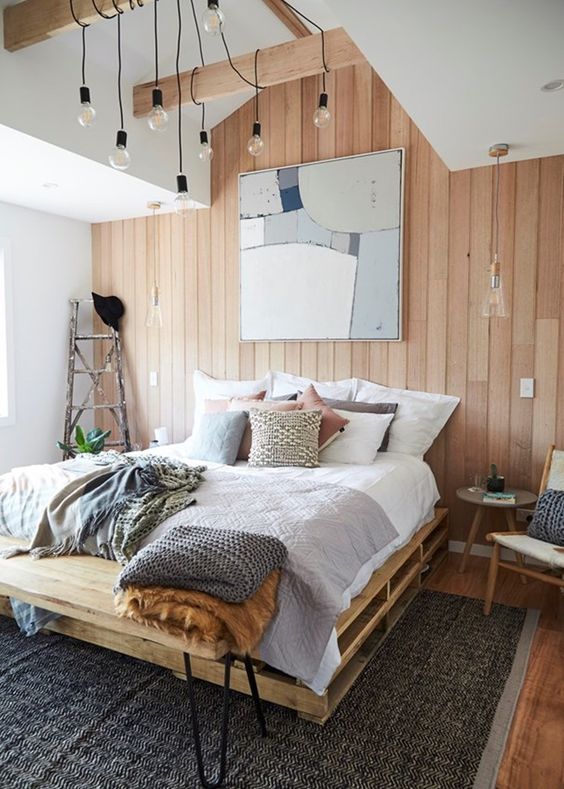 a Scandinavian bedroom with a stained accent wall, a pallet bed with neutral bedding, pendant bulbs, a chair and a ladder in the corner
