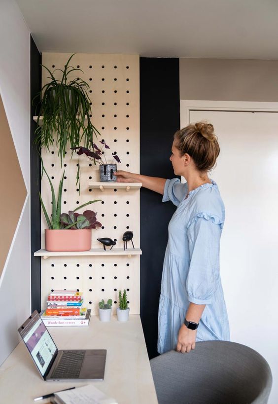 a Scandinavian home office with a pegboard with shelves, potted plants and some decor is a great space to work in