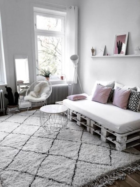 a Scandinavian living room with a white pallet sofa and pillows, a rug, a white chair, a coffee table and some decor
