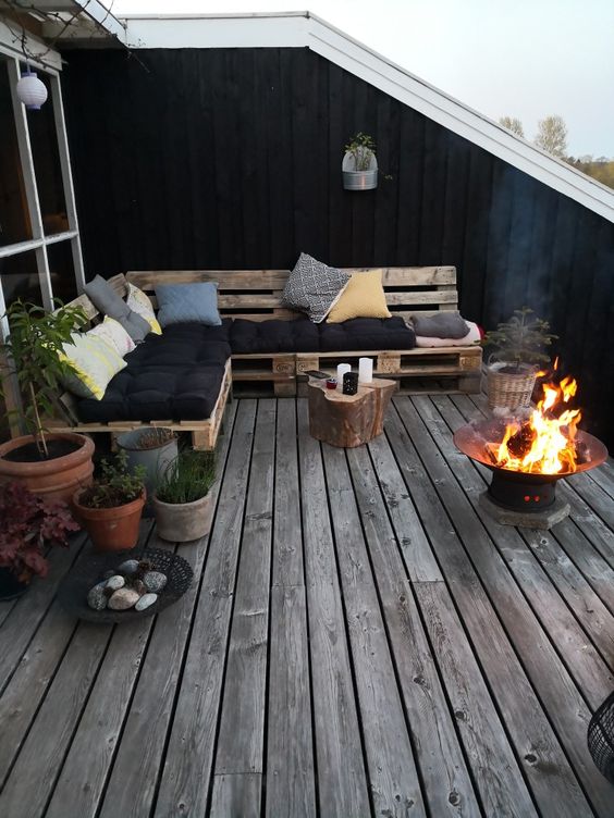 a Scandinavian terrace with a pallet sectional and some pillows, a fire bowl, potted plants and candles and pretty decor