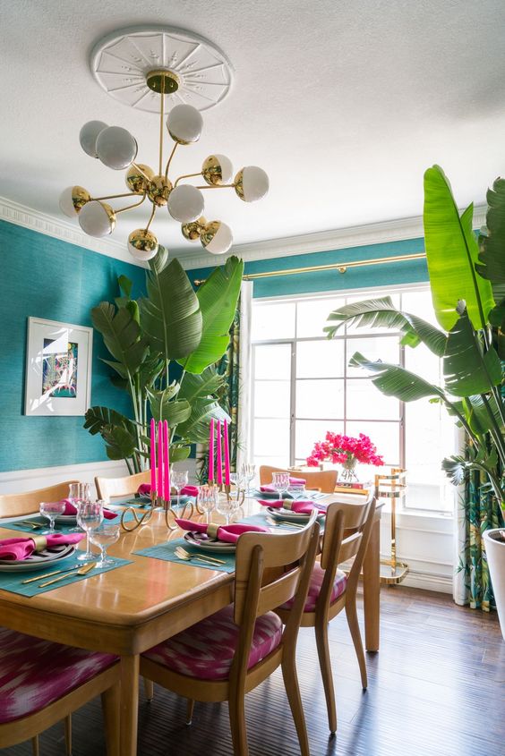 a beautiful and bold dining room with emerald walls, a table and pink chairs, colorful decor and a potted plant