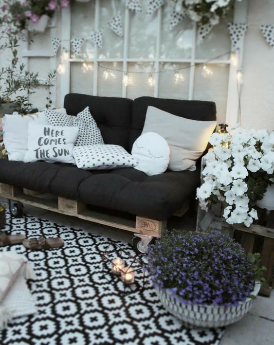 a black and white terrace with a pallet sofa on casters, black and white cushions and pillows, lights, potted blooms and candles