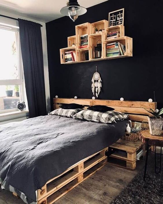 a black bedroom with a pallet bed and monochromatic bedding, a crate shelf, pendant lamps and potted plants