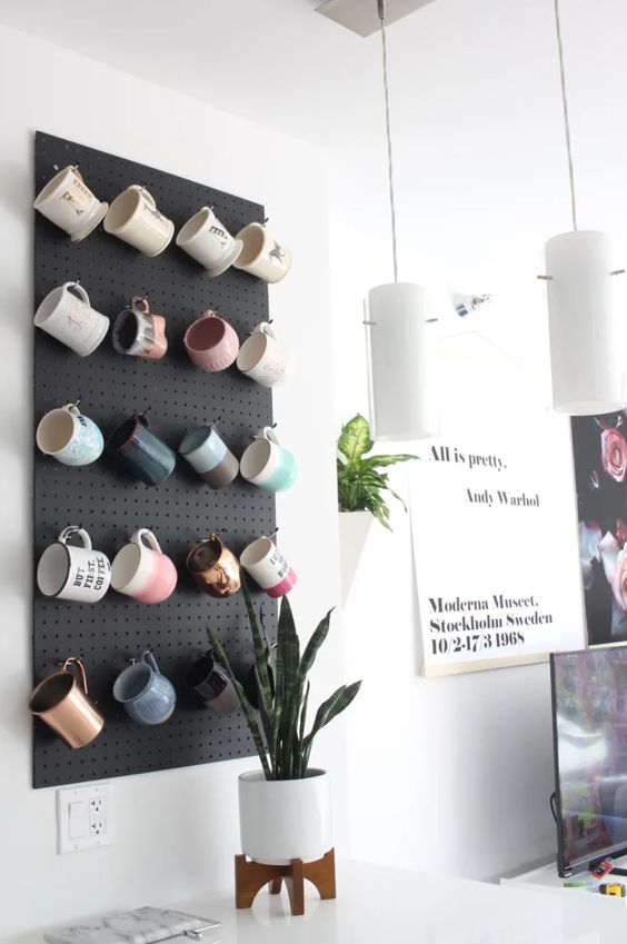 a black pegboard with hooks is used for organizing the mug collection, it looks chic, cool and stylish