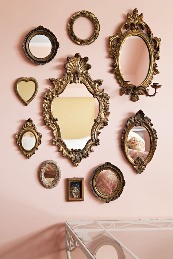 a blush wall with a gallery wall of vintage mirrors in various mismatching frames is amazing
