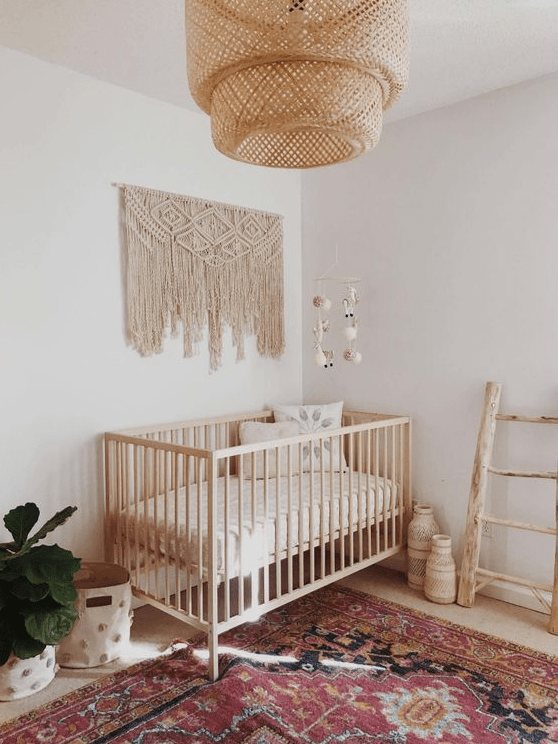 a boho baby's room with a wicker lampshade, a macrame hanging, a boho rug and a ladder