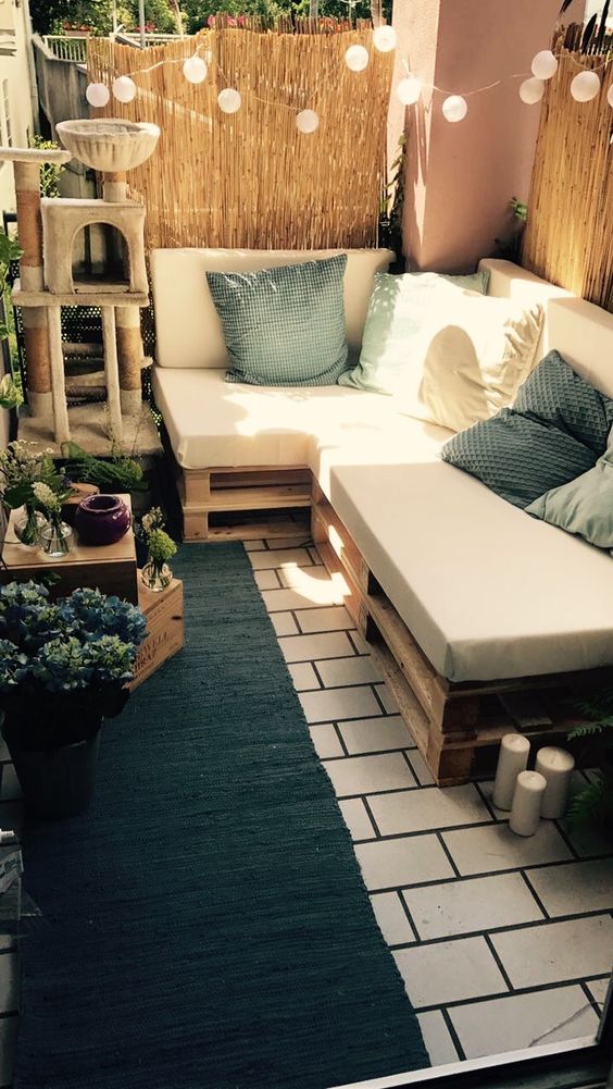 a boho balcony with a pallet corner sofa and pillows, lights, a rug and potted greenery plus a cat tree is amazing