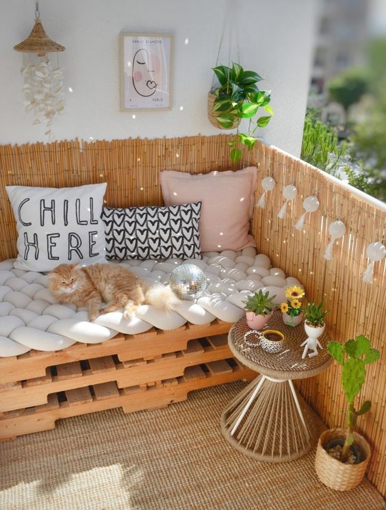a boho balcony with a pallet loveseat and pillows, a wicker table, some decor and potted plants is amazing