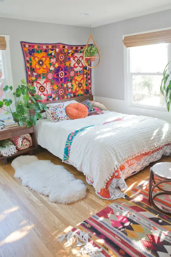 a boho bedroom with a bed and colorful bedding, a colorful boho rug, bright rugs on the floor and potted greenery