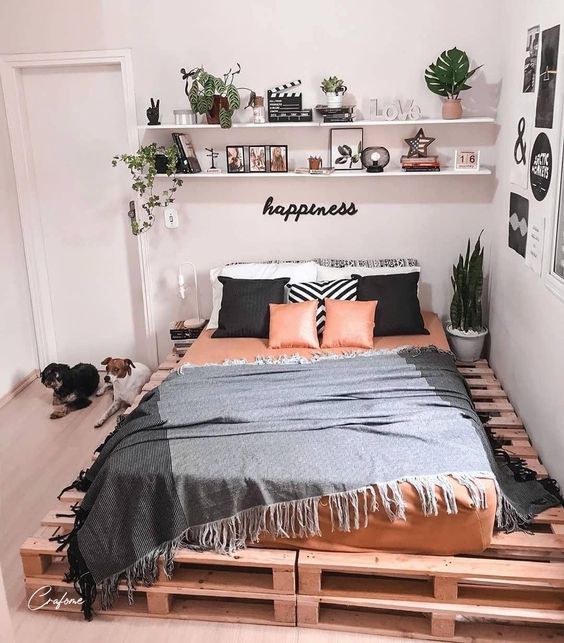 a boho bedroom with a pallet bed and bright bedding, shelves with decor and lamps and a black and white gallery wall