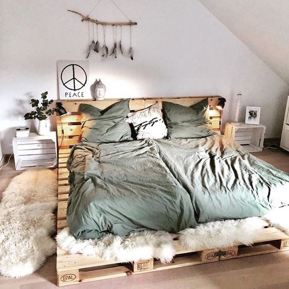 a hippie bedroom with a pallet bed and green bedding, crate nightstands, some faux fur, some lovely boho decor