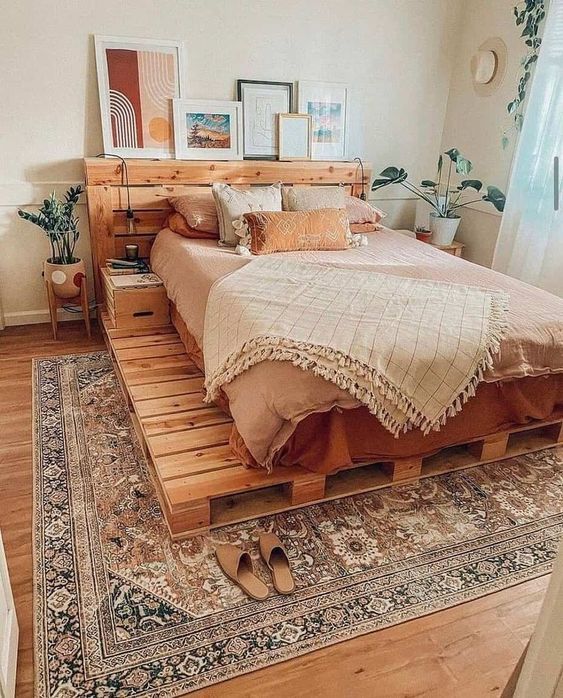 a boho bedroom with a pallet bed and neutral bedding, a boho rug, some plants and a headboard gallery wall
