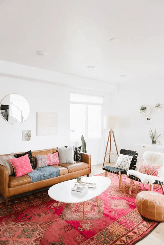 a boho living room with a a bright rug, a tan leather couch, colorful pillows, black woven chairs plus a coffee table