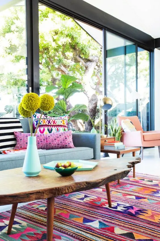 a boho living room with a blue sofa and pillows, a bold boho rug, a living edge table and a coral chair