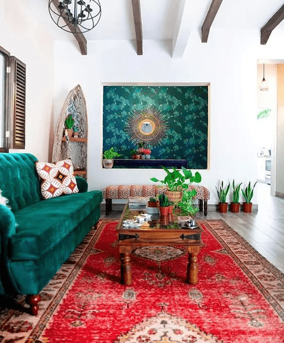 a boho living room with a bright red rug, an emerald sofa, a bold artwork and potted greenery and a stained coffee table