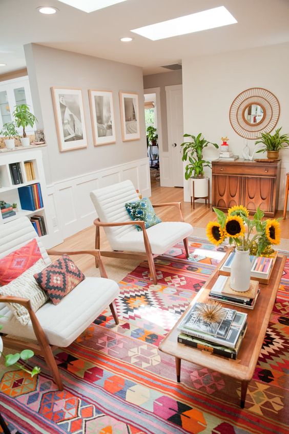 a boho living room with a stained console table, a bookshelf, white chairs, colorful pillows and a rug and a gallery wall