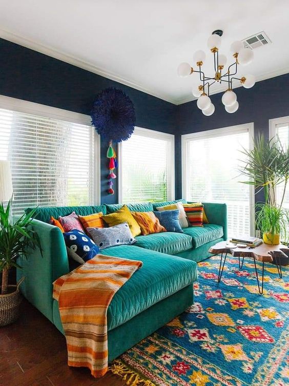 a boho living room with navy walls, a green sofa with colorful pillows, a colorful boho rug, a living edge table and some greenery