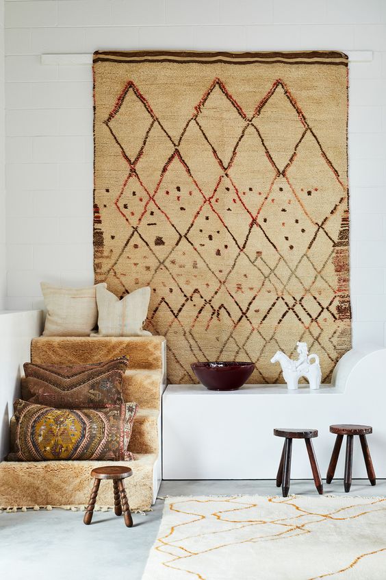 a boho space with a boho rug on the wall, some built-in furniture, some decor and stools is cool