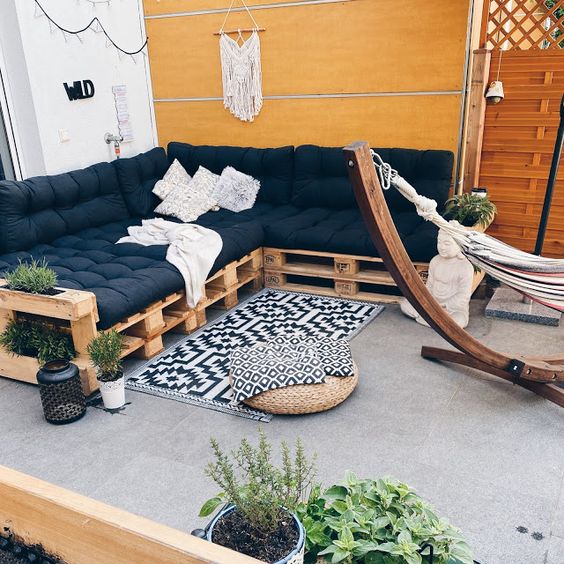 a boho terrace with a pallet sectional, black cushions and pillows, a boho rug and a jute pouf plus some potted greenery