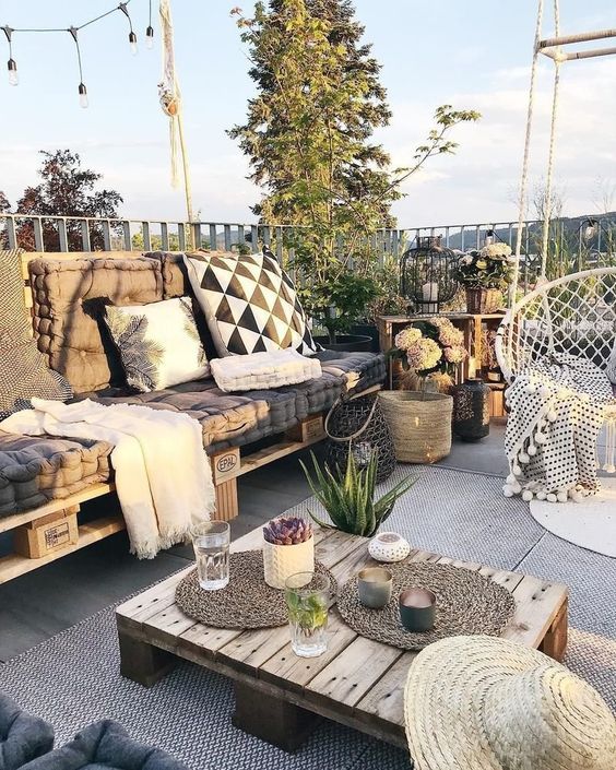 a boho terrace with a pallet sofa, a pallet coffee table, boho pillows, a pendant chair and some decor and plants