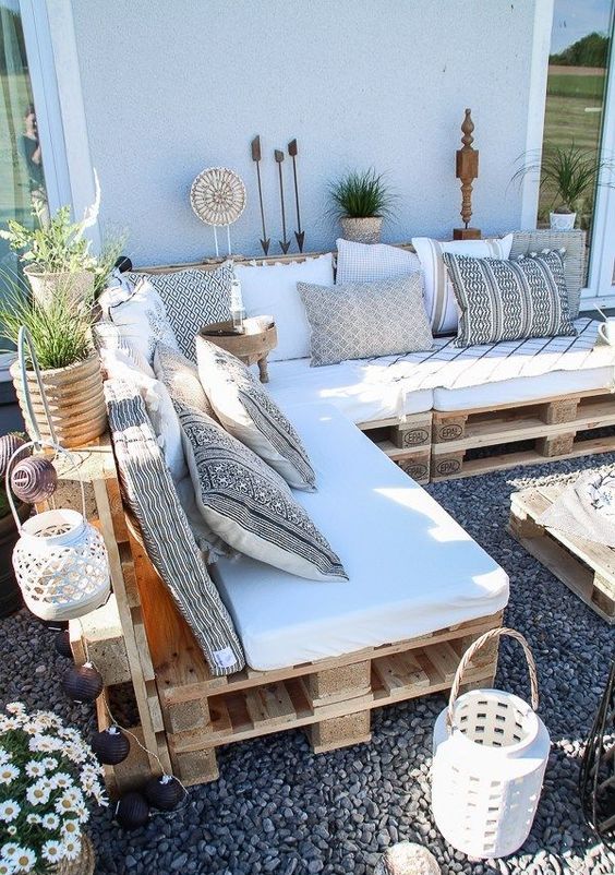 a boho terrace with a pallet sofa and boho pillows, potted greenery, candle lanterns and a pallet coffee table