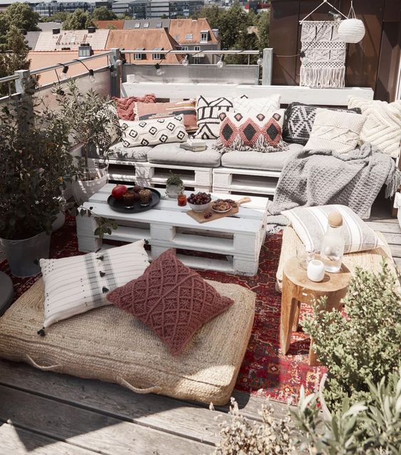 a boho terrace with a pallet sofa and coffee table, wooden stools and jute cushions plus lots of greenery around
