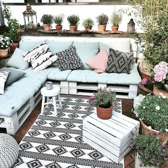 a boho terrace with a white pallet sofa, boho pillows, a crate, potted greenery and blooms is a lovely space
