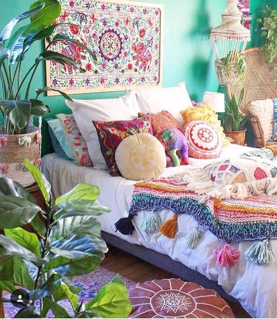 a bold boho bedroom with emerald walls, a bold rug on the wall, a bed with colorful beddng, some potted statement plants and decor