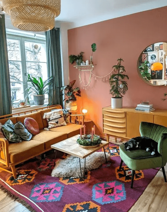 a bold eclectic living room with a muave accent wall, an orange sofa, a bold rug, a coffee table, a stained dresser, green curtains, potted plants