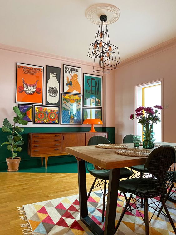 a bold modern dining room with a green color block wall and floor, a colorful rug, a bright gallery wall and some blooms