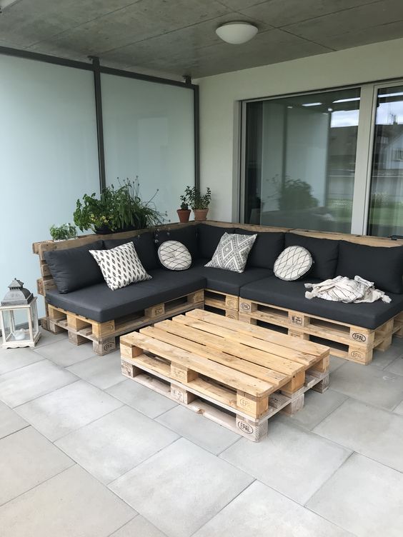 a bold terrace with a pallet corner sofa in black and with pillows, a pallet coffee table and potted greenery