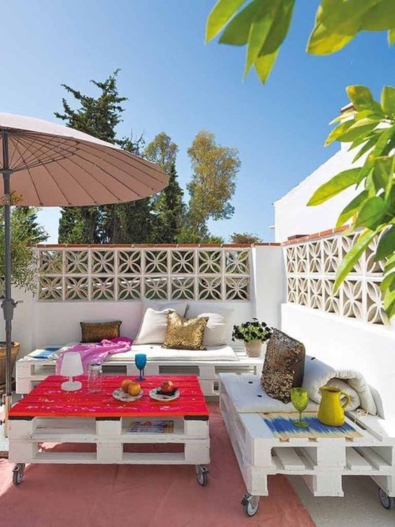 a bold terrace with a pallet sofa, a bench and a coffee table, colorful pillows and bold decor plus a pink rug