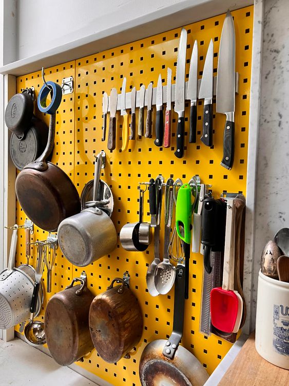 a bold yellow pegboard with all kinds of cookware and knives is a great idea for a modern kitchen, it looks bold and veyr eye-catching