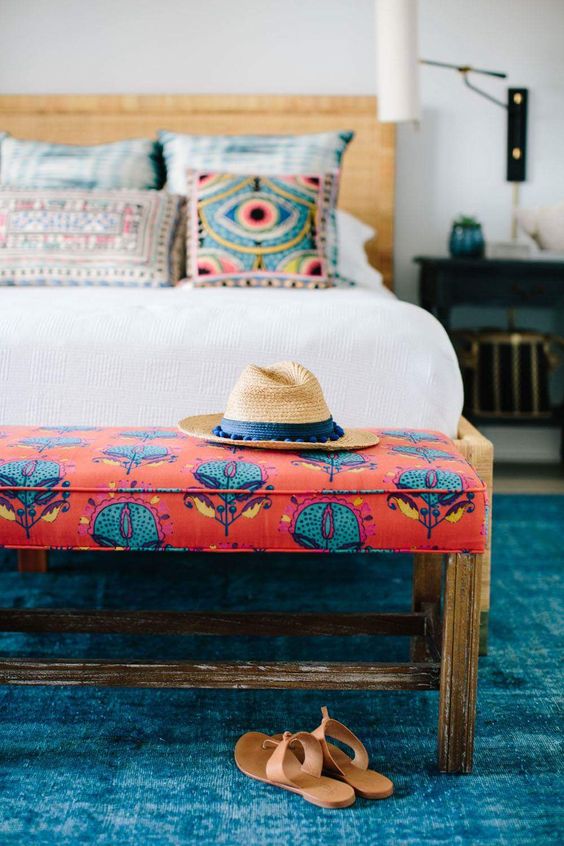 a bright bedroom with a woven bed and a colorful bench, a blue rug and some gold touches is a lovely space
