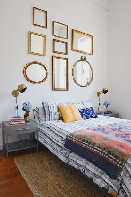 a bright bedroom with grey nightstands, bright bedding, a gallery wall of mirrors in gold frames is adorable