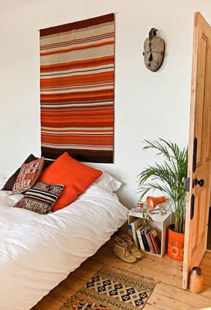 a bright boho bedroom with a colorful boho rug on the wall and a boho rug on the floor, a bed with printed pillows, a potted plant and some decor