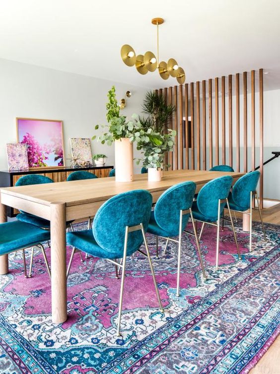 a bright dining room with a colorful rug, teal chairs, bright artwork and some elegant brass touches
