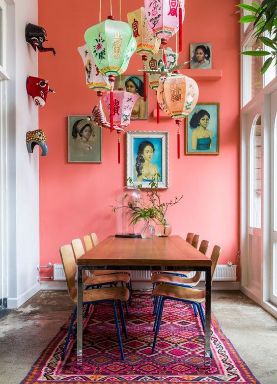 a bright dining room with a red wall, a table and chairs, colorful paper lamps, bold art, faux taxidermy and a colorful rug