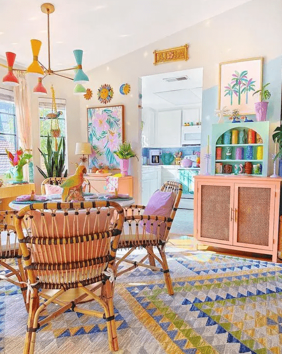 a bright dining room with a table and rattan chairs, a bold rug, a pink cabinet and turquoise shelves, a pastel chandelier
